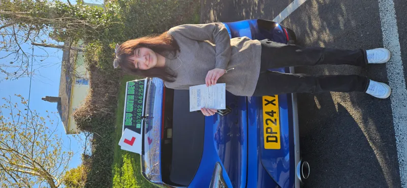 Student holding pass certificate next to Rev with Kev car after automatic driving test