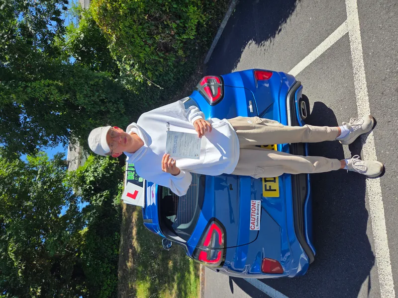 Student holding pass certificate next to Rev with Kev driving school car on sunny day