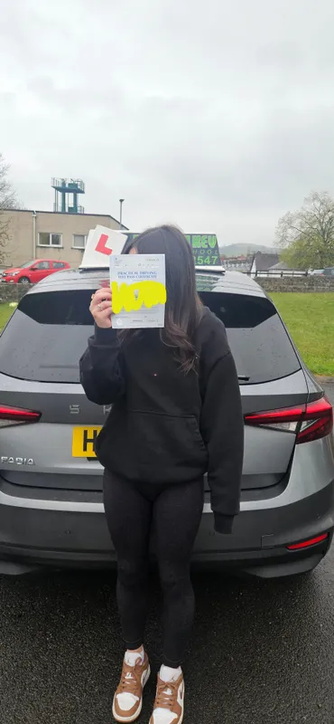 Student showing driving test pass certificate beside grey Rev with Kev car